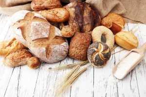 Assortment of baked bread and bread rolls on wooden table backgr
